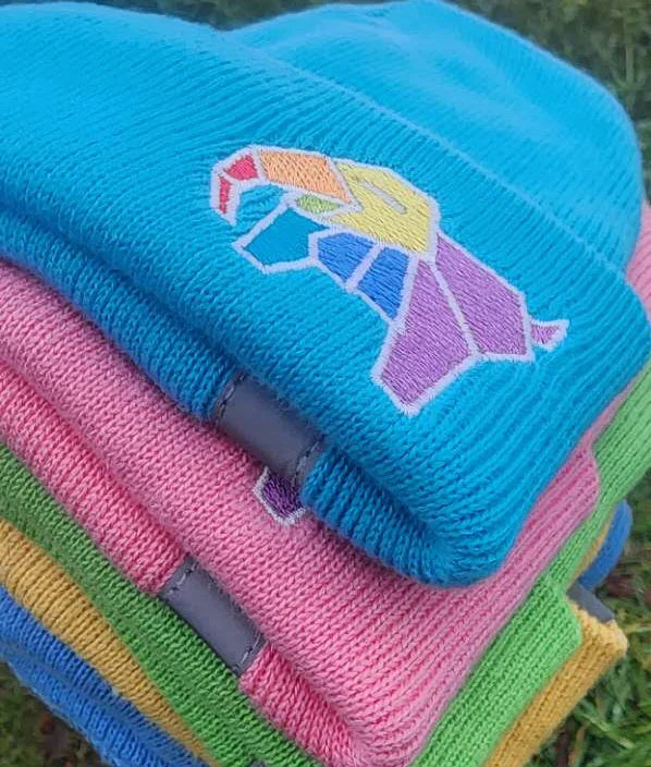 Stack of colorful knitted hats with embroidered designs on a grassy background